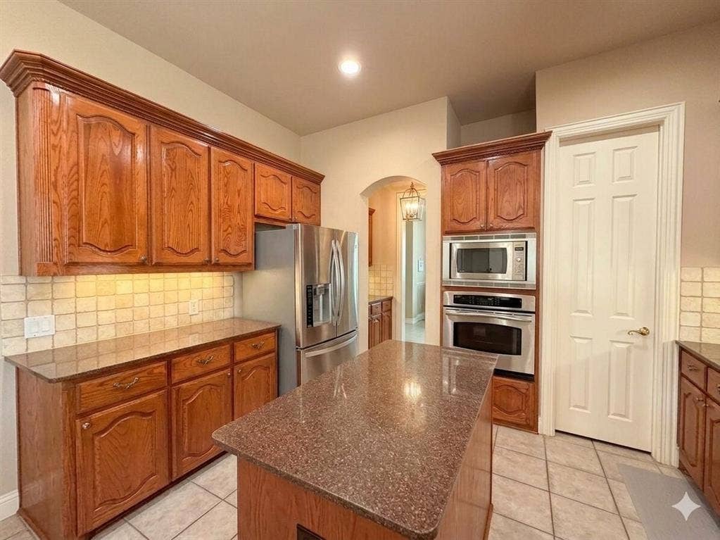 15031 Woodbluff Drive, Frisco, TX 75035 Kitchen featuring wood cabinetry, stainless steel appliances, a center island with a stone-finish countertop, and tile flooring