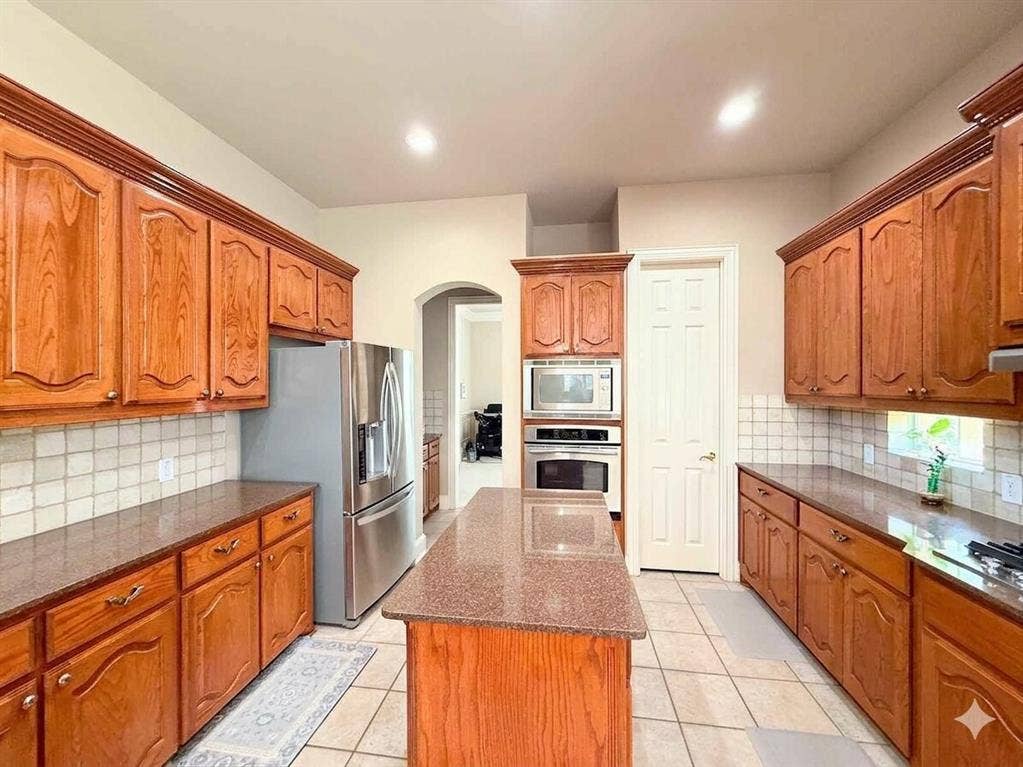 15031 Woodbluff Drive, Frisco, TX 75035 Kitchen featuring wood cabinetry, integrated stainless steel appliances, a center island with countertop, and tile flooring