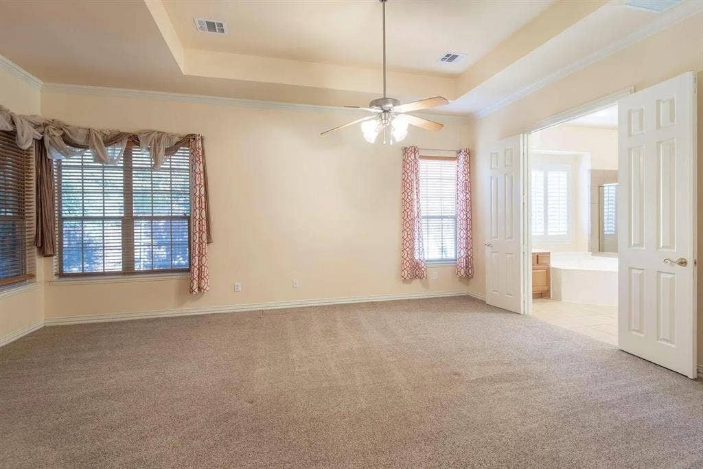 15031 Woodbluff Drive, Frisco, TX 75035 Spacious carpeted room featuring a tray ceiling with a ceiling fan, multiple windows with blinds, and double doors opening to an adjoining space with a built-in tub