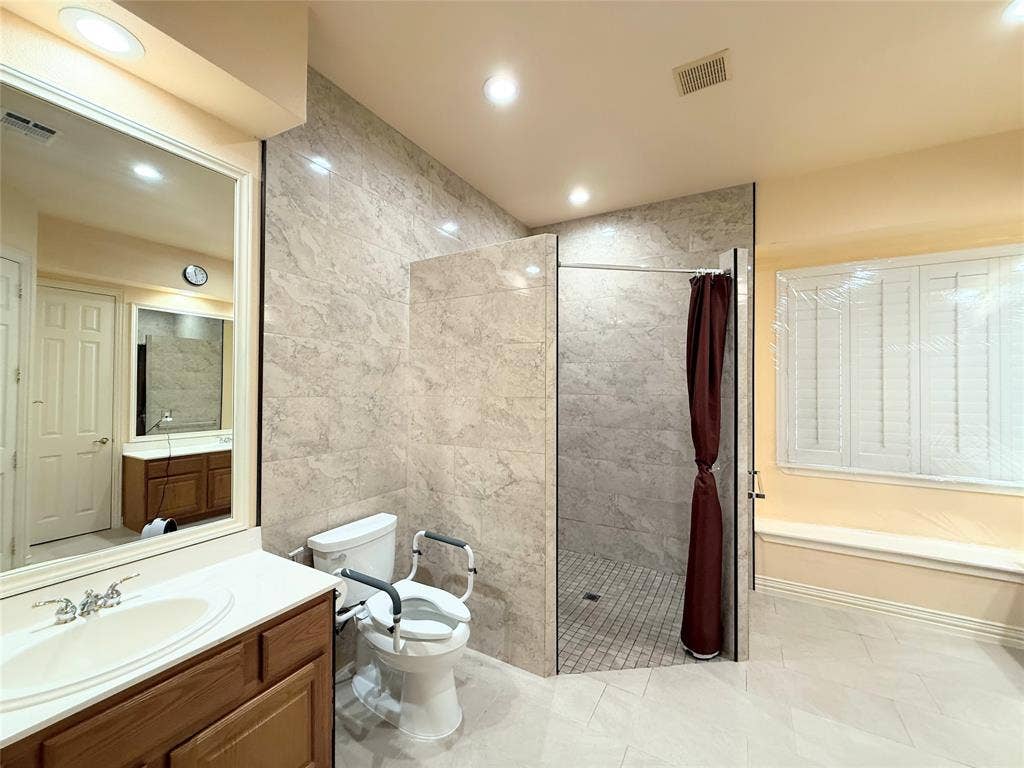 15031 Woodbluff Drive, Frisco, TX 75035 Bathroom featuring a walk-in shower with tile walls, a vanity with a white countertop, and a window with white shutters