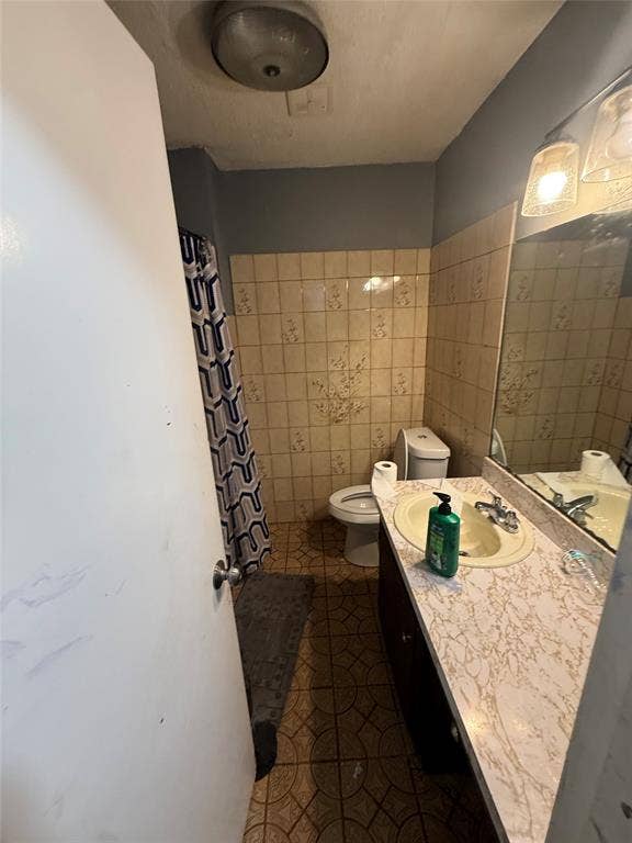 6036 Harrison Way, Watauga, TX 76148 Full bath featuring vanity, a shower with shower curtain, tile walls, and dark tile patterned floors