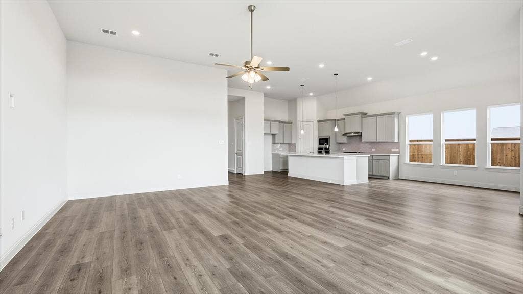 331 Fire Blade Drive, Aledo, TX 76008 Open-concept living area featuring wood-finish flooring, a contemporary kitchen with a large island, stainless steel appliances, pendant lighting, and multiple windows