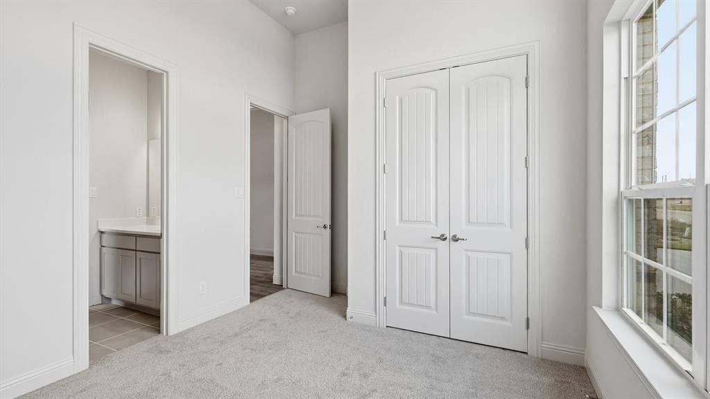 331 Fire Blade Drive, Aledo, TX 76008 Carpeted room featuring a double-pane window with white trim, a double-door closet with paneling, and an entryway to a bathroom with a vanity and tile flooring