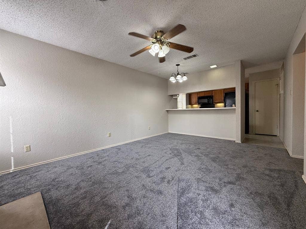 1723 Crest Grove Drive, #120B, Arlington, TX 76012 Unfurnished living room featuring ceiling fan, dark colored carpet, a chandelier, a textured ceiling, and a textured wall