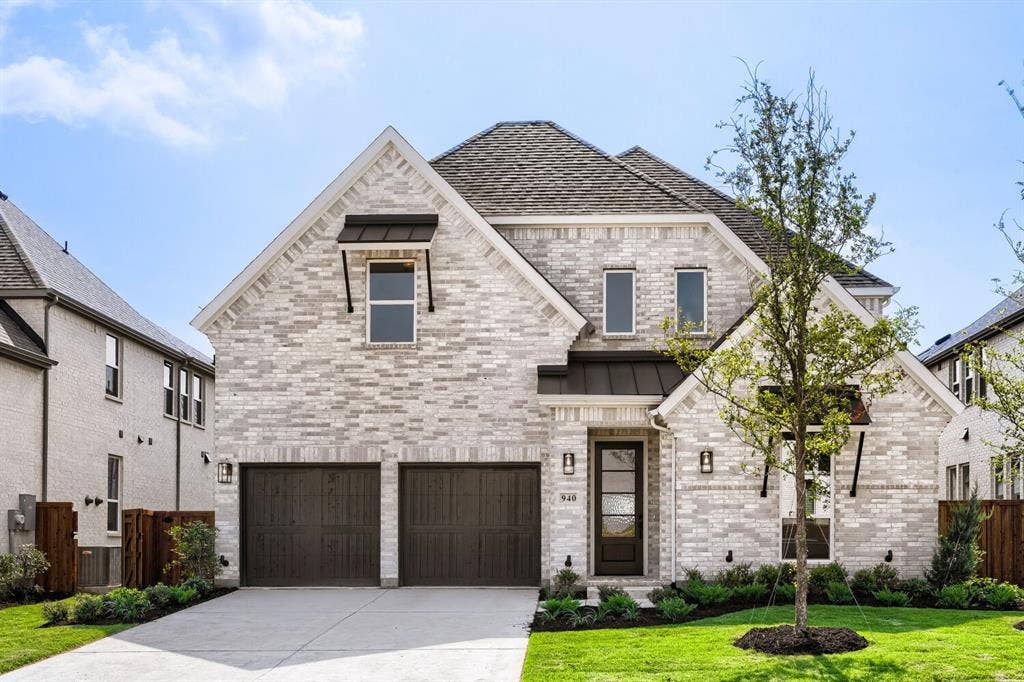 940 Heatherbrook Drive, Prosper, TX 75078 Brick facade home featuring a two-car garage, dark wood-finish garage doors, dark metal awnings, and a covered entry with a dark door