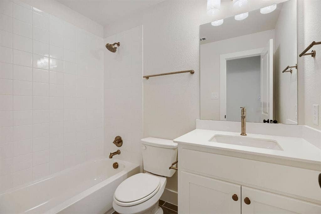 940 Heatherbrook Drive, Prosper, TX 75078 Bathroom featuring a white subway tile tub surround, white vanity with an integrated sink, vanity mirror, bronze-finish fixtures, and dark tile flooring