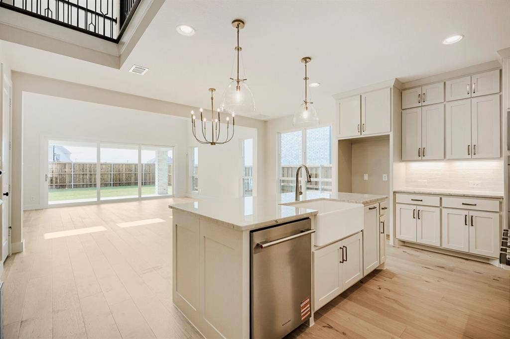 940 Heatherbrook Drive, Prosper, TX 75078 Open-concept kitchen and living area featuring light wood-finish flooring, a kitchen island with a farmhouse sink, stainless steel dishwasher, and quartz countertops