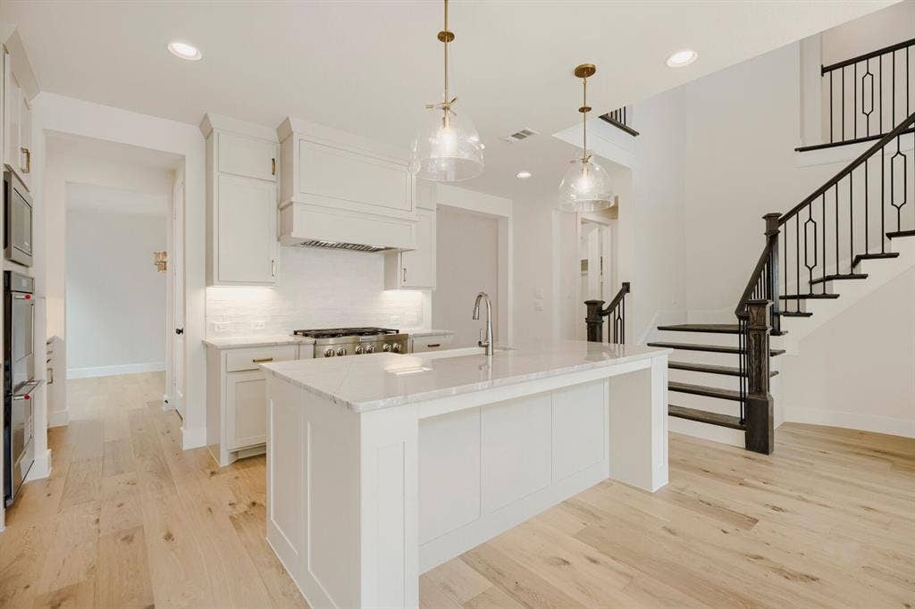 940 Heatherbrook Drive, Prosper, TX 75078 Modern kitchen featuring a large central island with a sink, white cabinetry with gold hardware, stainless steel appliances, and a tile backsplash