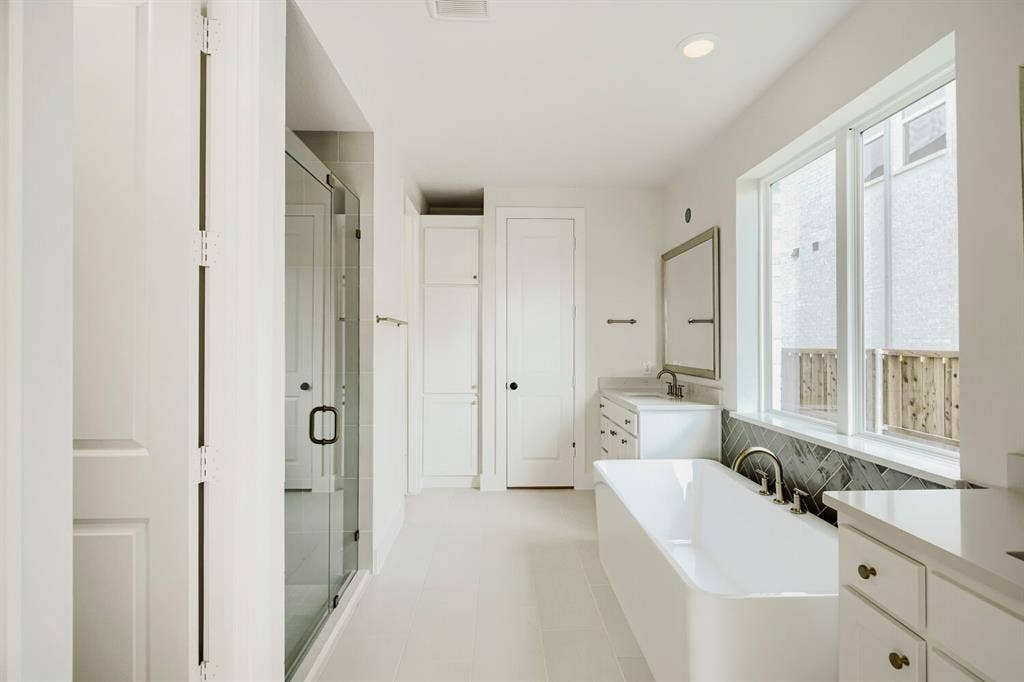 940 Heatherbrook Drive, Prosper, TX 75078 White bathroom featuring a freestanding tub, glass-enclosed shower, dual vanities with undermount sinks, and a herringbone tile accent wall