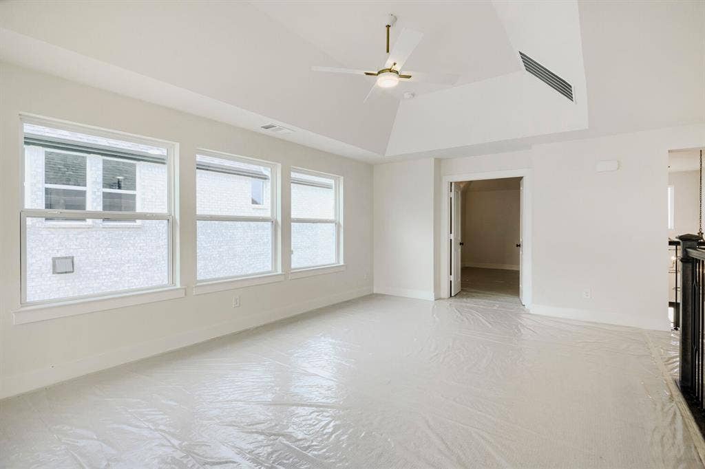 940 Heatherbrook Drive, Prosper, TX 75078 Spacious room featuring a vaulted ceiling with a modern ceiling fan, three large windows, white trim, and a doorway opening to an interior space