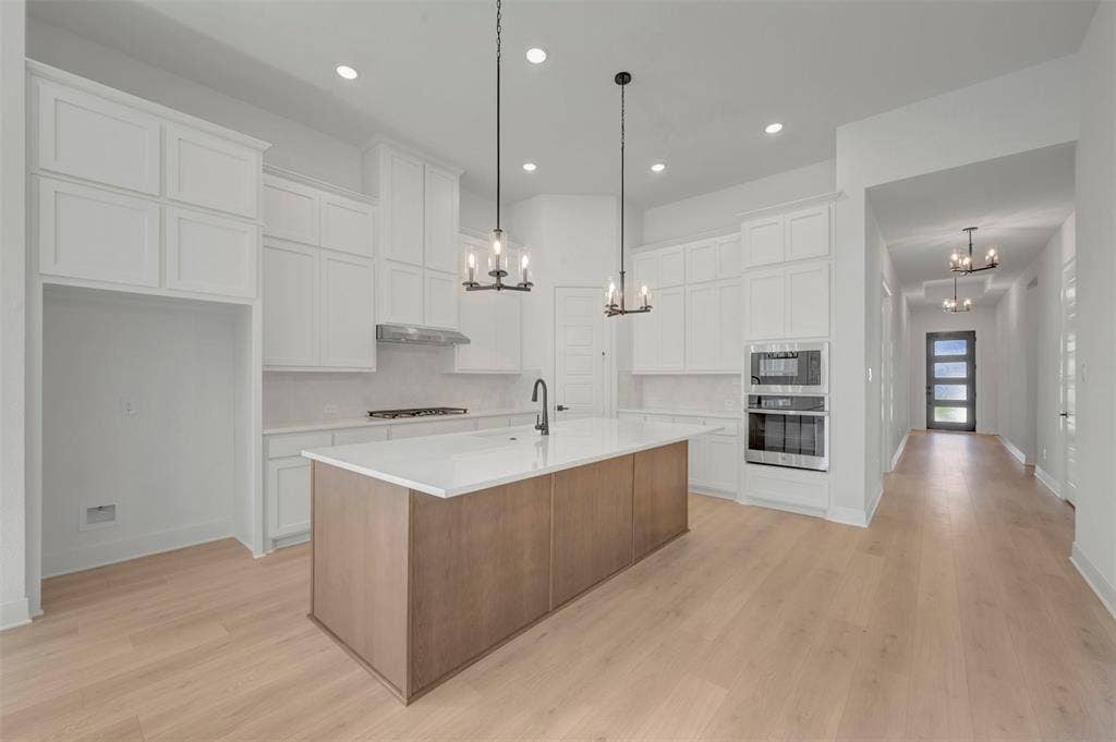 1709 Drover Street, Northlake, TX 76247 Modern kitchen featuring a large central island, light wood-finish flooring, white cabinetry, integrated double ovens, and recessed lighting
