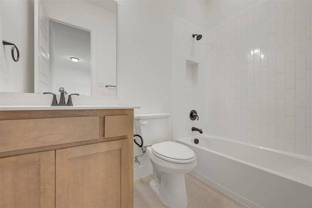 1709 Drover Street, Northlake, TX 76247 Bathroom featuring a light wood vanity with a white countertop, a rectangular mirror, a white toilet, and a bathtub with white subway tile surround and a recessed niche