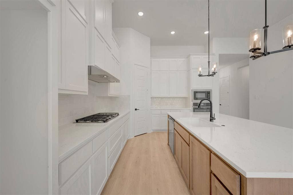 1709 Drover Street, Northlake, TX 76247 Modern kitchen featuring a large central island with an integrated sink and matte black faucet, stainless steel dishwasher, white countertops, a gas cooktop with range hood, and light wood-finish flooring