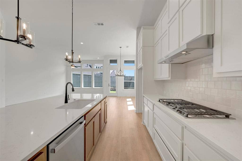 1709 Drover Street, Northlake, TX 76247 Contemporary kitchen featuring an expansive island with an undermount sink and matte black faucet, light wood-finish flooring, white shaker cabinetry, a gas cooktop, and a subway tile backsplash