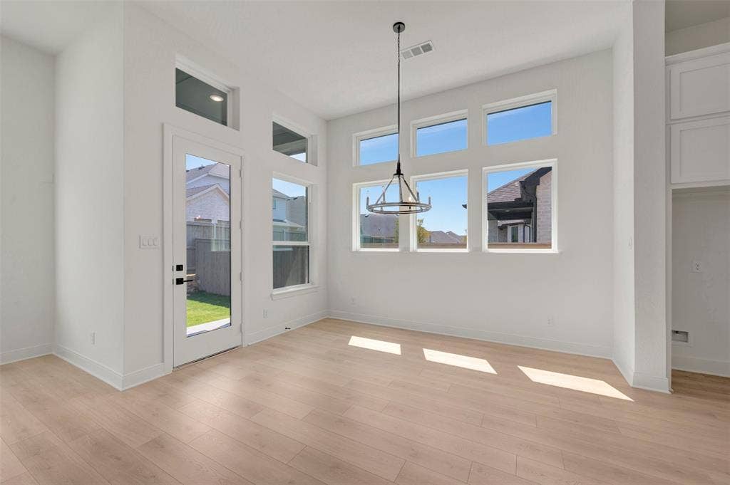 1709 Drover Street, Northlake, TX 76247 Spacious room featuring light wood-finish flooring, a contemporary chandelier, multiple transom windows, a glass-paneled exterior door, and built-in white cabinetry