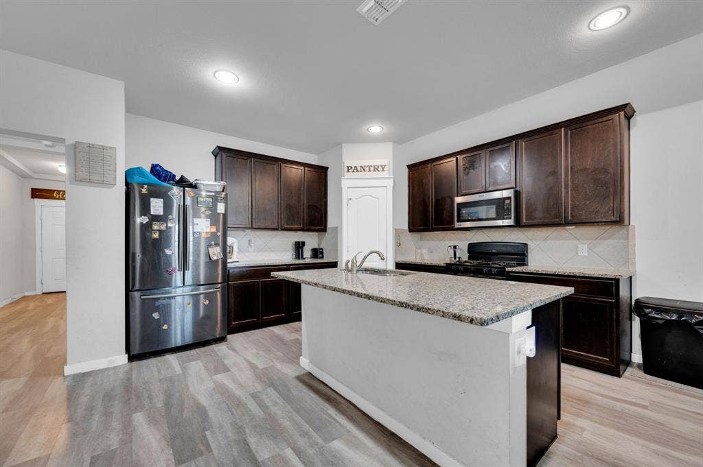 2609 Centurion Road, Glenn Heights, TX 75154 Kitchen with stainless steel appliances, dark wood finish cabinets, an island with sink, light stone countertops, and backsplash