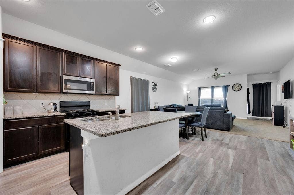 2609 Centurion Road, Glenn Heights, TX 75154 Kitchen featuring light stone counters, dark wood finish cabinets, open floor plan, an island with sink, and recessed lighting