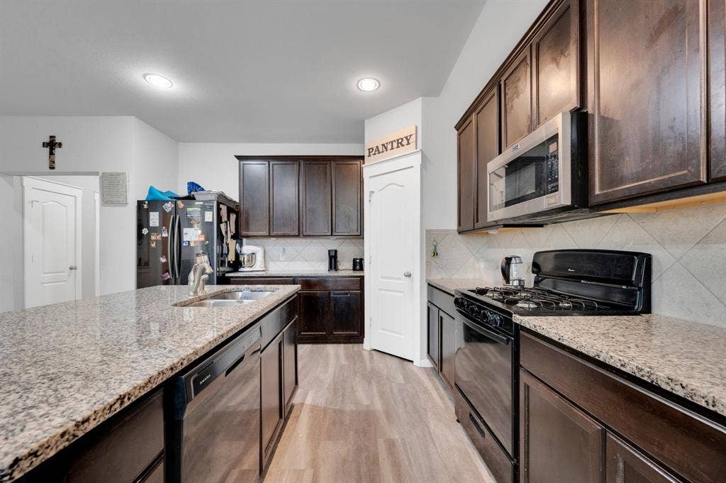 2609 Centurion Road, Glenn Heights, TX 75154 Kitchen featuring black range with gas stovetop, dark wood finish cabinetry, dishwasher, stainless steel microwave, and light wood-type flooring