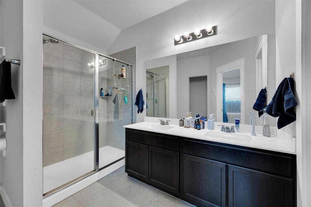 2609 Centurion Road, Glenn Heights, TX 75154 Bathroom featuring double vanity, lofted ceiling, a shower stall, and light tile patterned flooring