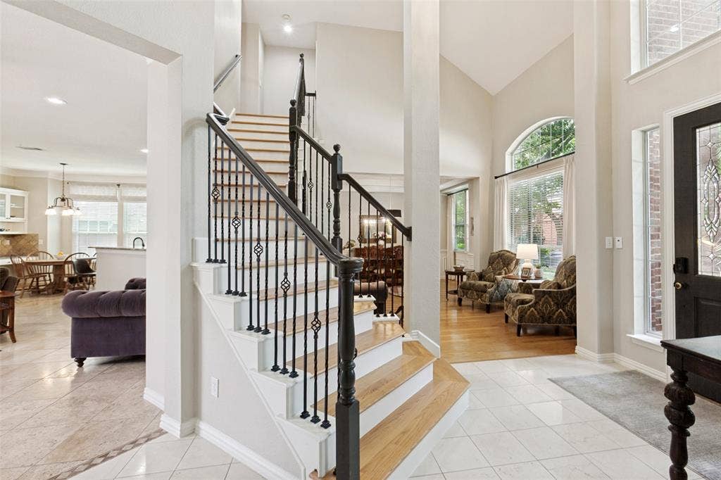 2632 Barrington Drive, Plano, TX 75093 Foyer with tile flooring featuring a decorative border, a prominent staircase with wood treads and wrought iron balusters, and an arched window providing natural illumination