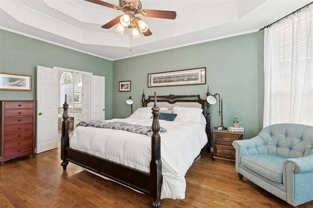 2632 Barrington Drive, Plano, TX 75093 Private first floor primary bedroom suite featuring wood-finish flooring, a tray ceiling with a built-in fan light fixture, and white double doors opening to a spacious bathroom enhanced with a large walk-in closet
