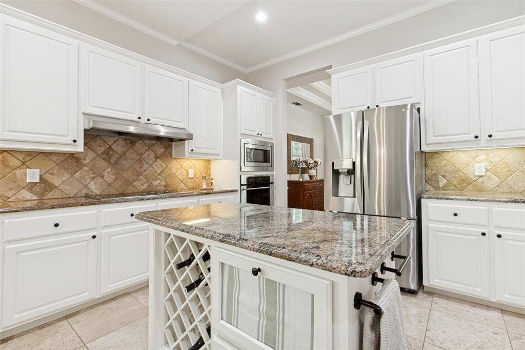 2632 Barrington Drive, Plano, TX 75093 Spacious kitchen featuring white cabinetry, granite countertops, a diamond-patterned tile backsplash, stainless steel appliances, and a central island with integrated wine storage