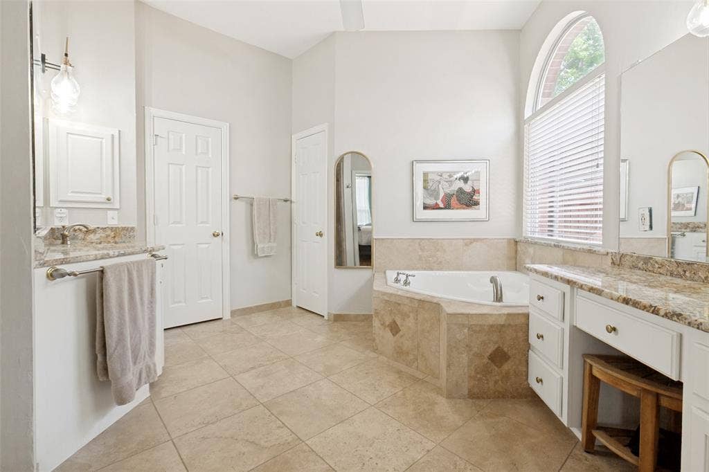 2632 Barrington Drive, Plano, TX 75093 Spacious bathroom featuring a corner jetted tub, arched window, dual vanity areas with granite countertops, walk-in closet, and tile flooring