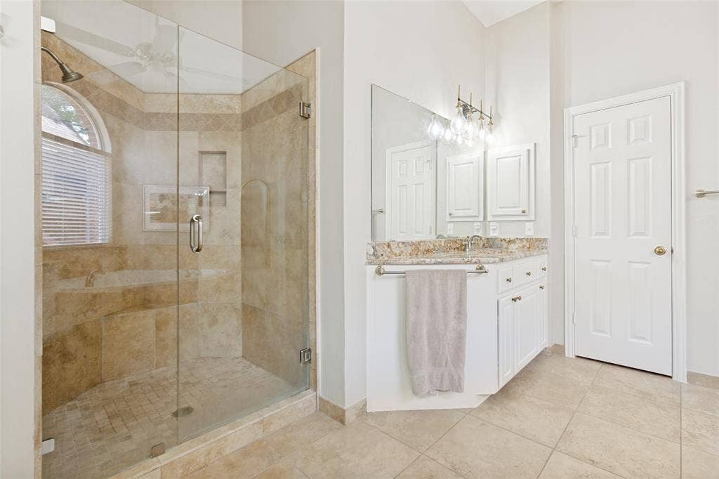 2632 Barrington Drive, Plano, TX 75093 Spacious bathroom featuring a glass-enclosed shower with stone tile, an arched window, and a built-in bench