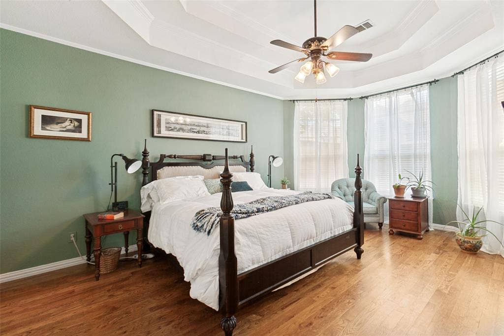 2632 Barrington Drive, Plano, TX 75093 First floor primary bedroom suite featuring wood-finish flooring, a tray ceiling with crown molding, and a ceiling fan.