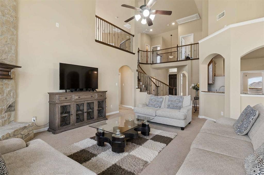 2446 Old Stables Drive, Celina, TX 75009 Living area with a ceiling fan, arched walkways, carpet flooring, a high ceiling, and a stone fireplace