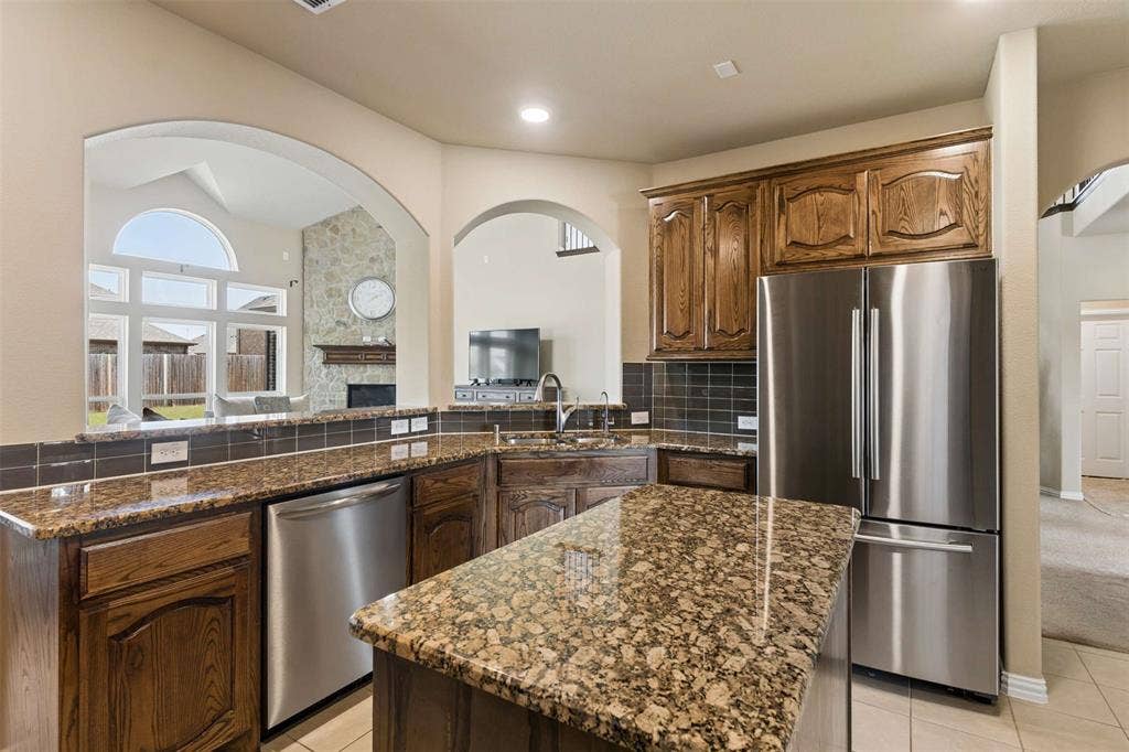 2446 Old Stables Drive, Celina, TX 75009 Kitchen with stainless steel appliances, dark stone countertops, a fireplace, backsplash, and light tile patterned flooring