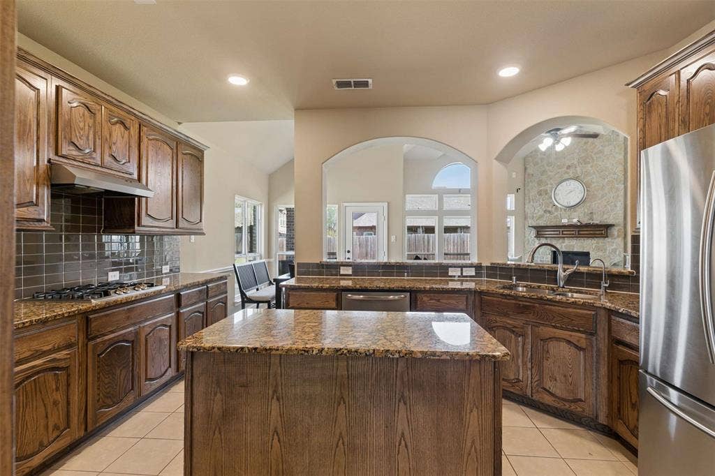 2446 Old Stables Drive, Celina, TX 75009 Kitchen with decorative backsplash, a center island, dark stone counters, a stone fireplace, and recessed lighting
