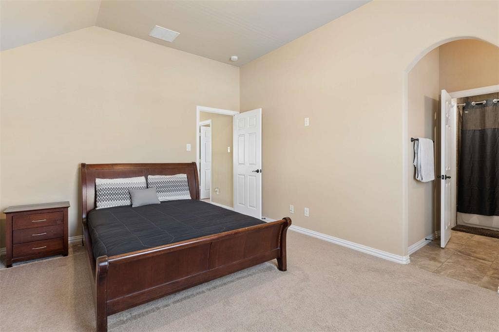 2446 Old Stables Drive, Celina, TX 75009 Bedroom featuring light colored carpet, arched walkways, connected bathroom, and vaulted ceiling