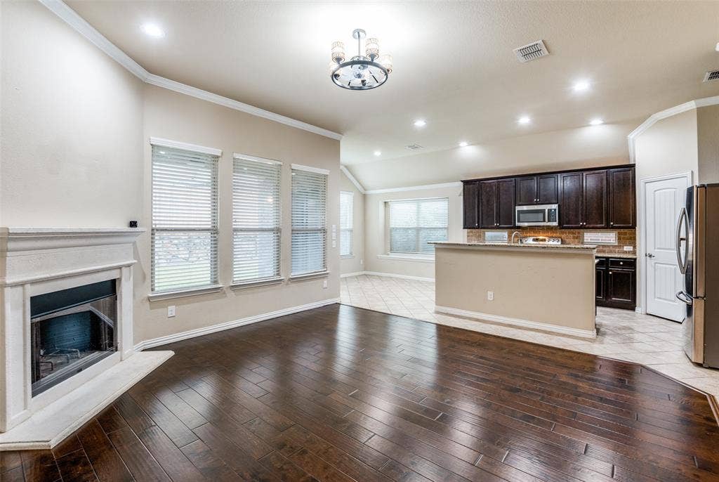 16425 Toledo Bend Court, Prosper, TX 75078 Unfurnished living room featuring ornamental molding, a fireplace with raised hearth, lofted ceiling, a chandelier, and light wood-style flooring