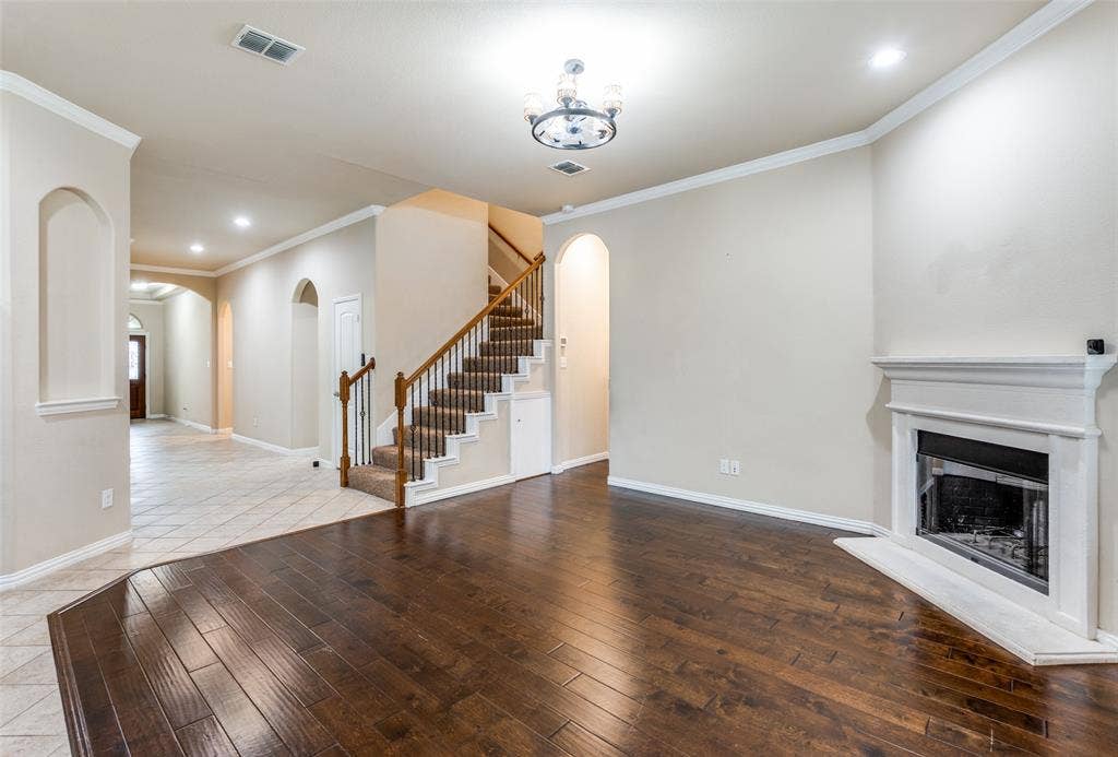 16425 Toledo Bend Court, Prosper, TX 75078 Unfurnished living room featuring arched walkways, ornamental molding, hardwood / wood-style flooring, a fireplace with raised hearth, and recessed lighting
