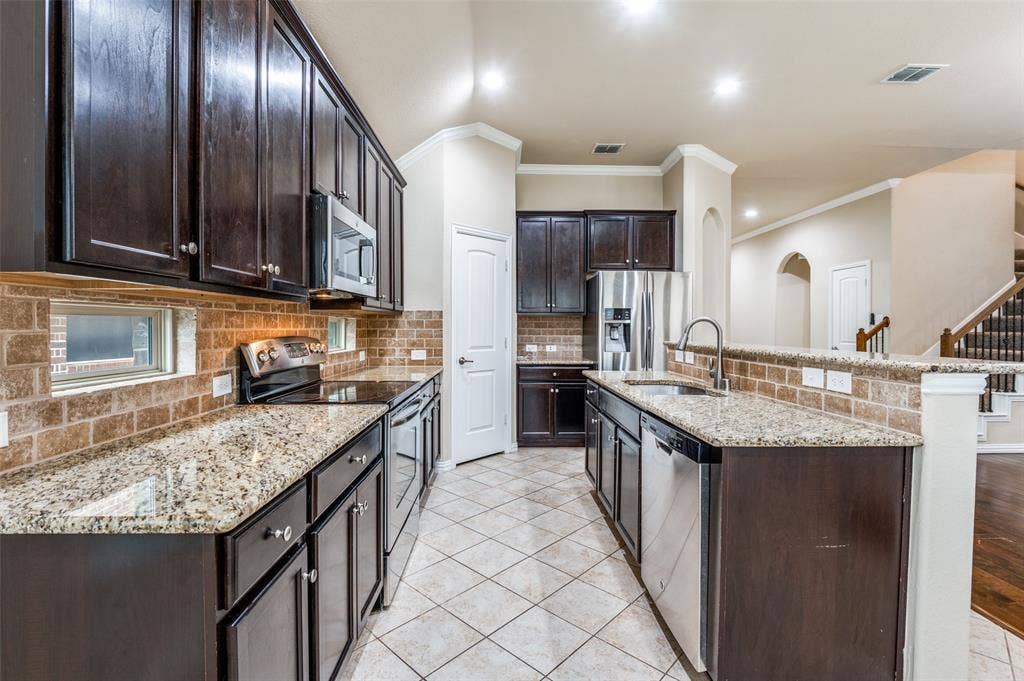 16425 Toledo Bend Court, Prosper, TX 75078 Kitchen with dark wood finish cabinetry, ornamental molding, stainless steel appliances, decorative backsplash, and light tile patterned floors