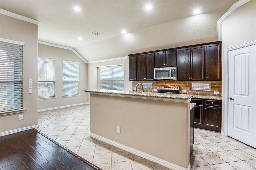 16425 Toledo Bend Court, Prosper, TX 75078 Kitchen featuring dark wood finish cabinetry, ornamental molding, vaulted ceiling, tasteful backsplash, and stainless steel appliances