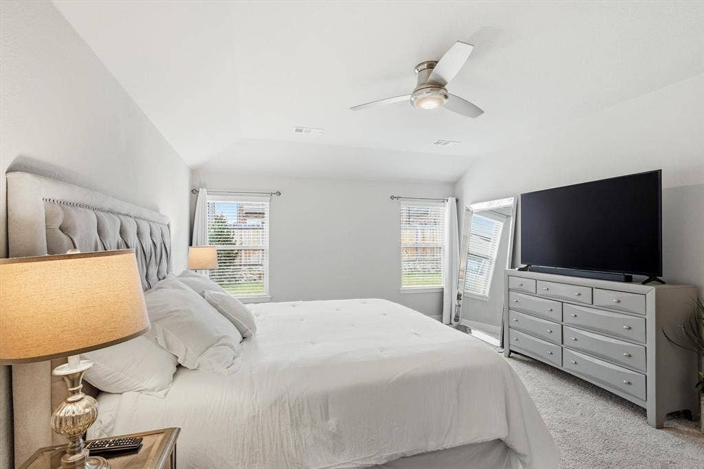 1212 Mount Olive Lane, Forney, TX 75126 Vaulted ceiling bedroom with a ceiling fan light fixture, two windows with blinds, and plush carpeting