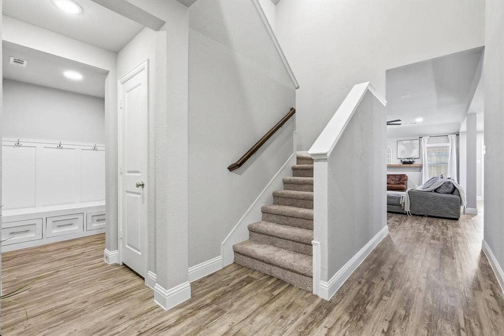 1212 Mount Olive Lane, Forney, TX 75126 Interior entryway with wood-finish flooring, a carpeted staircase with wood handrail, and built-in white cabinetry featuring storage hooks and drawers