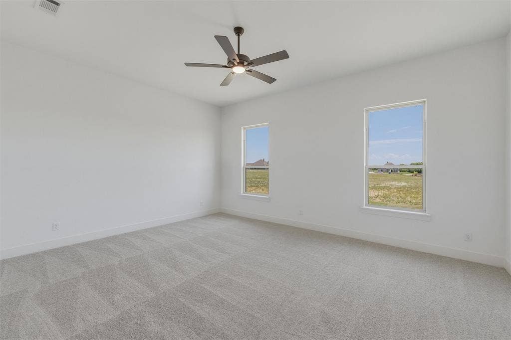 2408 Quartz Street, Krum, TX 76249 Spacious room featuring light gray patterned carpeting, white walls, two windows, and a ceiling fan with integrated lighting