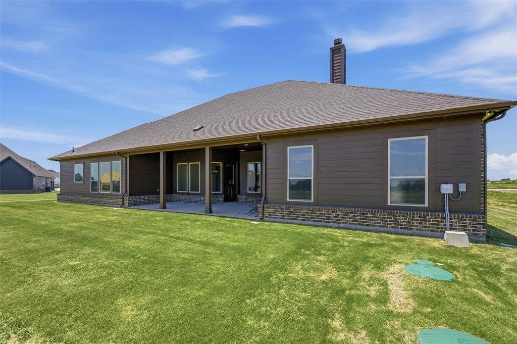 2408 Quartz Street, Krum, TX 76249 Expansive backyard featuring a covered patio, a full brick skirt, and a dark brown horizontal siding exterior