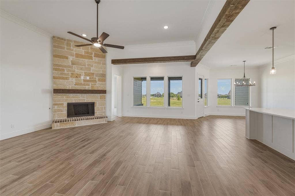 2408 Quartz Street, Krum, TX 76249 Spacious living area featuring a stone fireplace with a wood mantle, wood-finish flooring, vaulted ceilings with exposed wood beams, and multiple windows
