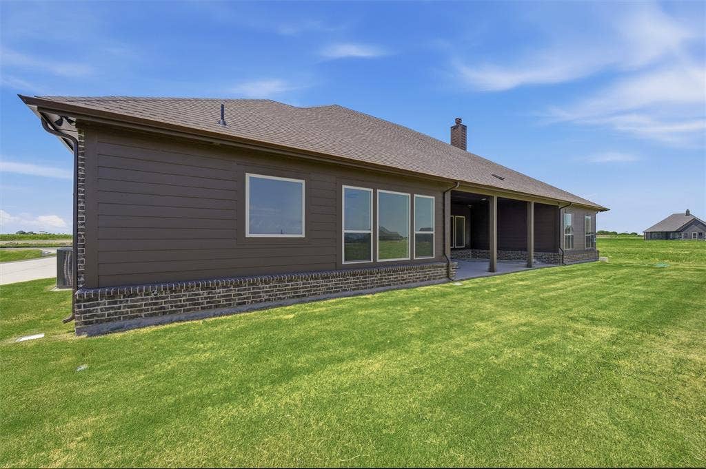 2408 Quartz Street, Krum, TX 76249 Expansive rear exterior featuring a covered patio, brick and siding facade, multiple windows, and a large grassy area