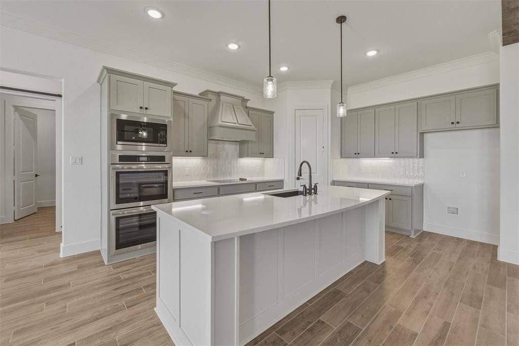 2408 Quartz Street, Krum, TX 76249 Modern kitchen featuring a large central island with a solid surface countertop, light gray cabinetry, stainless steel double ovens, and wood-finish flooring