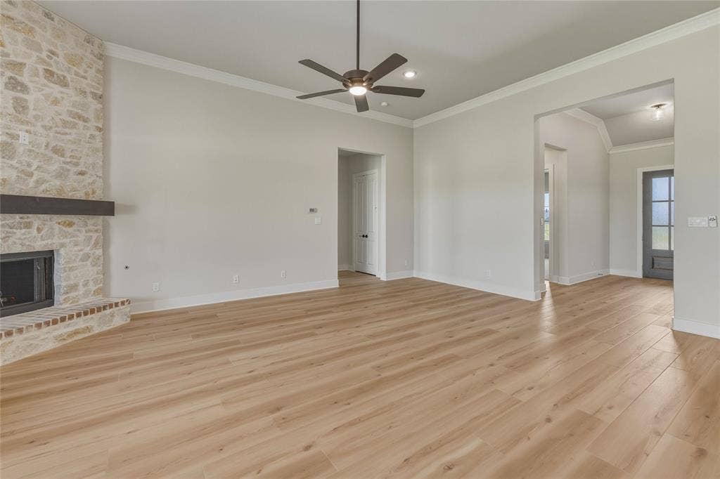 2305 Gypsum Street, Krum, TX 76249 Open-concept living area featuring light wood-finish flooring, a stone-clad fireplace with a wood mantel, crown molding, and a ceiling fan