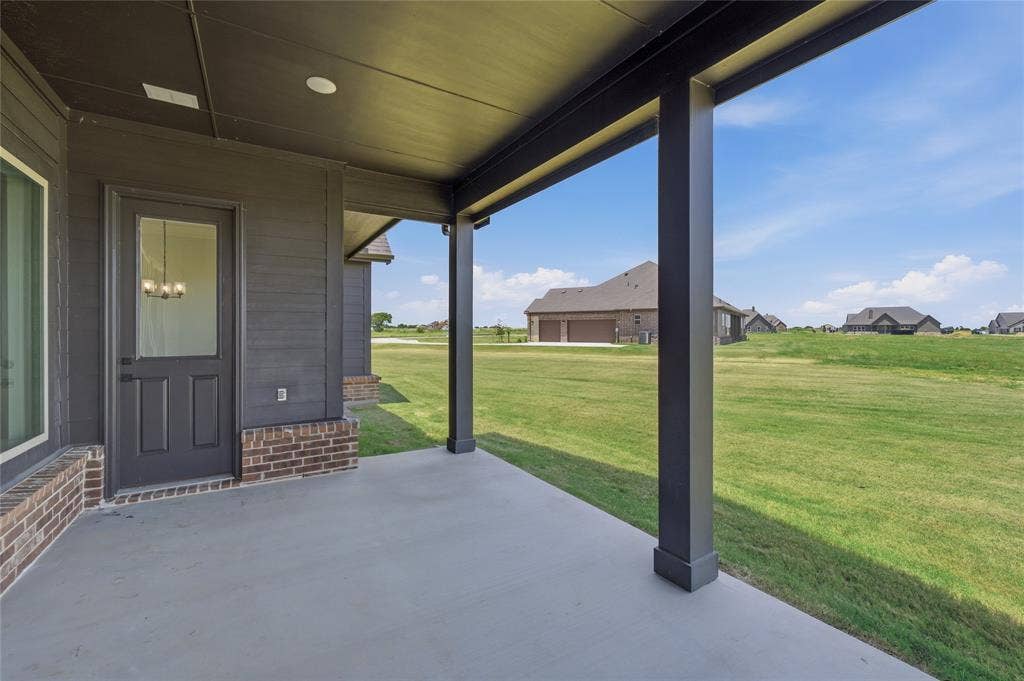 2305 Gypsum Street, Krum, TX 76249 Covered concrete patio featuring dark horizontal siding and a partial brick facade