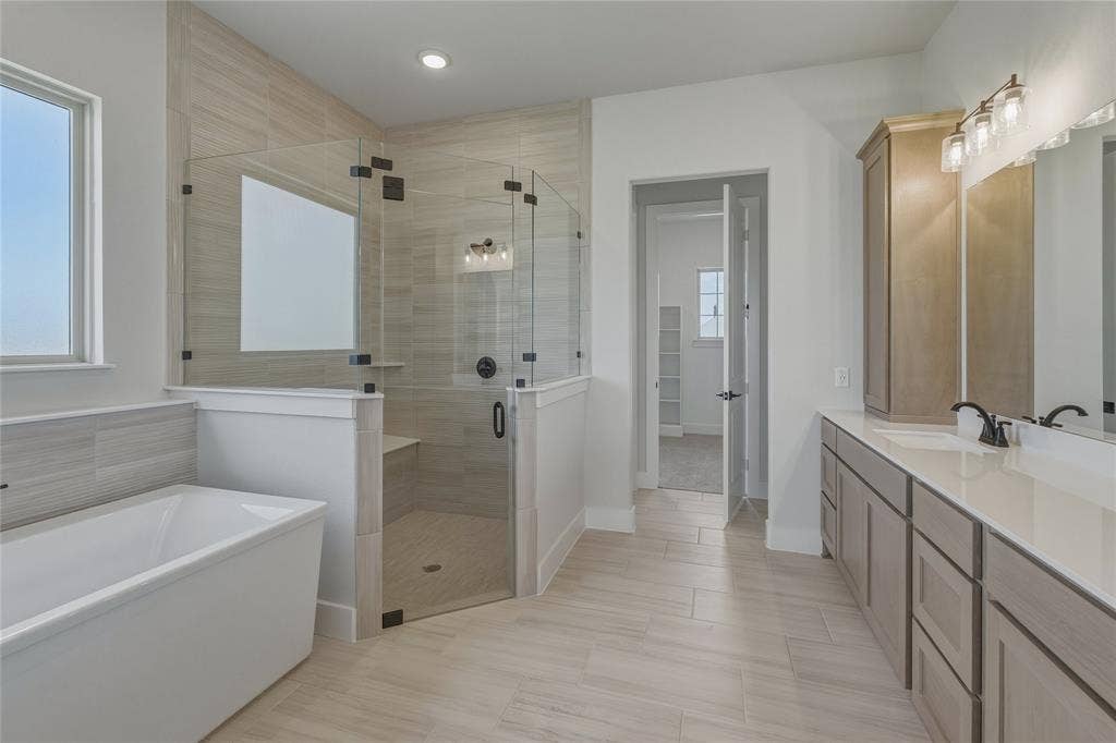 2305 Gypsum Street, Krum, TX 76249 Spacious bathroom featuring a freestanding tub, glass-enclosed shower with a bench, dual vanity, and light wood-finish cabinetry