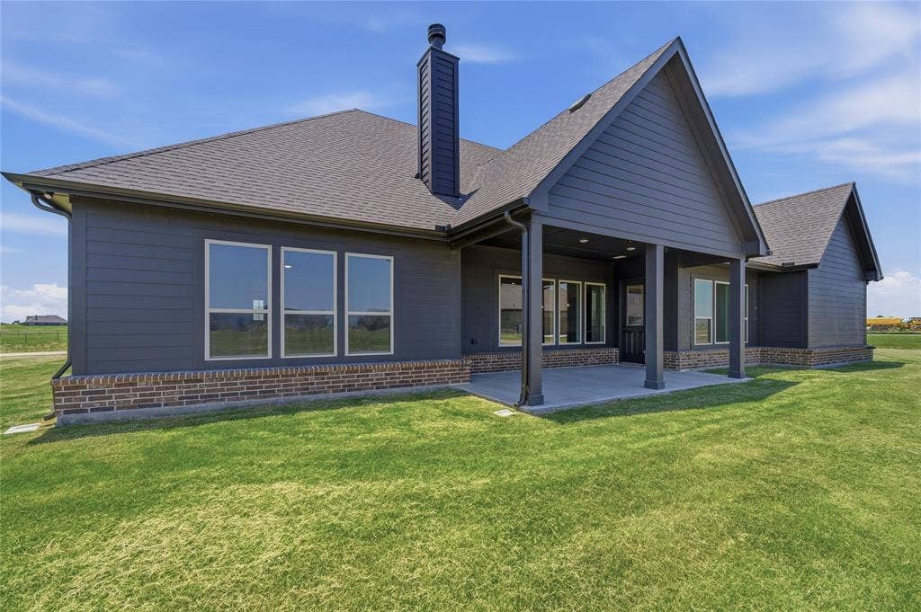 2305 Gypsum Street, Krum, TX 76249 Expansive green lawn surrounds a modern residence featuring dark siding and a prominent covered patio with supporting columns