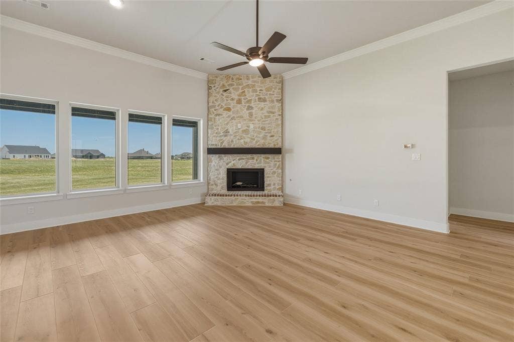 2305 Gypsum Street, Krum, TX 76249 Spacious room featuring a stone-clad corner fireplace with a dark wood mantel, wood-finish flooring, a contemporary ceiling fan, and a wall of four large windows