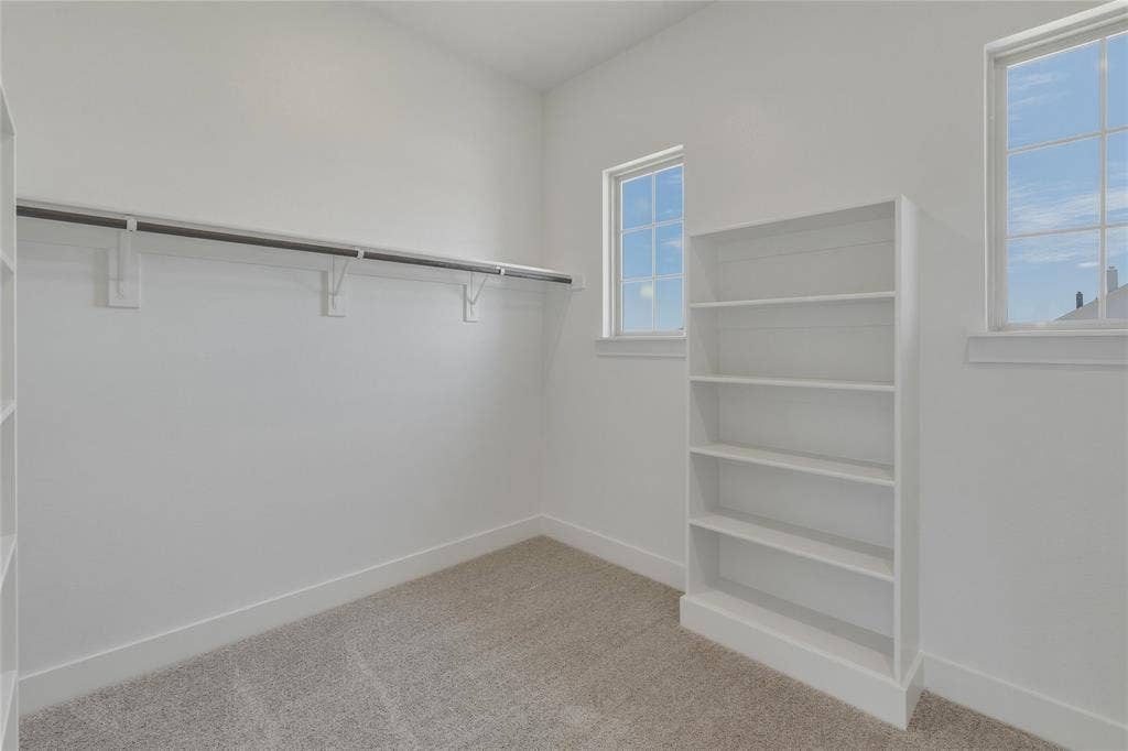 2305 Gypsum Street, Krum, TX 76249 Carpeted room with a built-in five-shelf bookcase, two single-hung windows, and a full-length clothes rod with shelving
